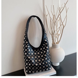 Detail of black leather hobo bag featuring silver punk rivets on a white book stand