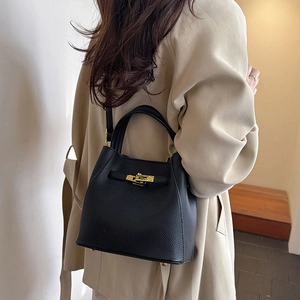 Black pebbled leather bucket bag with gold clasp shown on a model in a beige coat