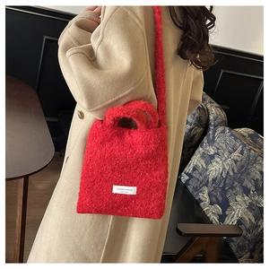 Detail of red plush tote bag with white woven label worn over a beige coat
