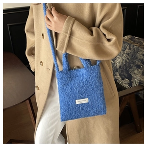 Blue fuzzy fleece handbag shown on model wearing a classic beige wool coat