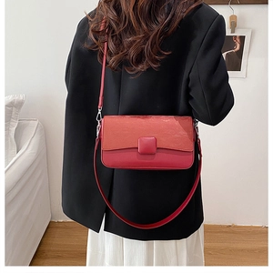 Red crossbody bag with textured flap and smooth leather finish on a black blazer