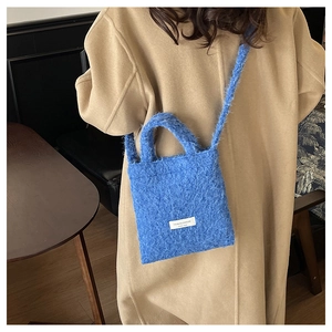 Close-up of vibrant blue wool shoulder bag with brand tag on model in camel coat