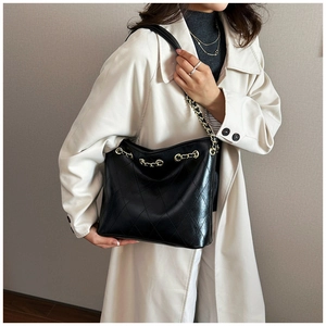 Model wearing black quilted tote bag with gold chain strap over a white trench coat