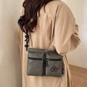 Detail van grijsgroene nylon crossbodytas met dubbele ritszakken en een touwriem
