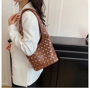 Detailed view of silver rivets on dark brown leather shoulder bag with wide strap