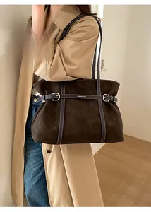 Detail of brown suede tote bag with white stitching and silver buckle held by a model