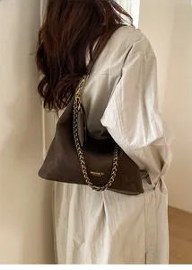 Detail of dark brown suede hobo bag with gold woven chain and logo on shoulder