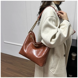 Detail of large quilted tote bag in brown leather worn with a beige trench coat
