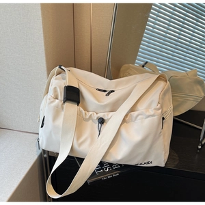 Detail view of cream travel bag with drawstring pocket and adjustable black shoulder strap