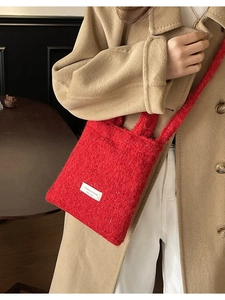 Red knit crossbody bucket bag styled with a wool coat in a warm indoor setting