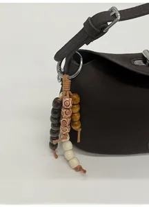 Detail of dark brown leather tote featuring a textured finish and multi-color wooden bead charm