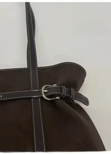 Close-up of dark brown leather tote bag featuring silver buckle and white contrast stitching
