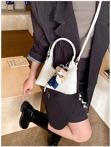 White crescent crossbody bag detail with cute blue bear charm on a slim leather strap