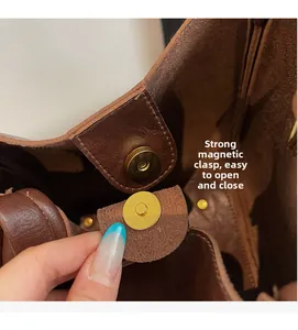 Close-up of the secure golden magnetic buckle closure on a brown leather bucket bag