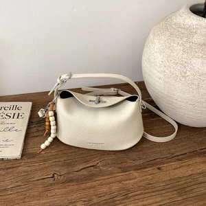 Detail view of cream leather crossbody bag with silver clasp and wooden bead charm