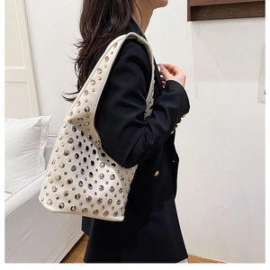 Detail of white hobo bag with silver rivets worn over the shoulder with a black blazer