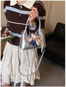 Silver metallic dumpling bag with teddy bear pendant shown in a lifestyle casual setting