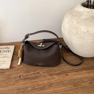 Detail view of lychee-textured dark brown leather handbag with elegant wooden bead charm
