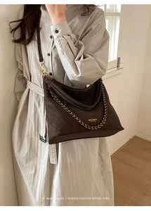 Detailed shot of dark brown suede tote with gold chain strap and brand logo