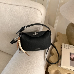 Detail of black lychee leather crossbody bag with silver twist lock and beaded charm pendant