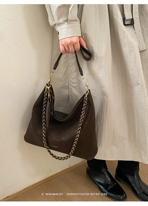 Detail of dark brown tote bag featuring gold brand logo and metal chain strap