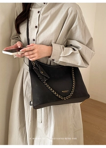 Detail of black tote bag featuring a textured gold chain strap and a small coin purse