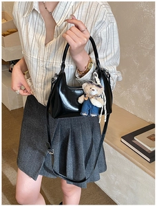 Detail of black glossy crescent bag with cute bear charm and adjustable leather strap