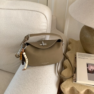 Close-up of khaki pebbled leather bag on sofa with wood bead charm and silver clasp