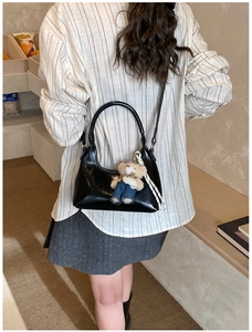 Glossy black hobo bag with a cute teddy bear pendant shown in a shoulder carry style