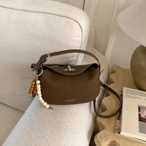Detail of dark brown pebble leather handbag with gold lettering and beaded charm