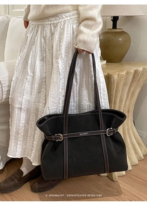 Detail of black tote bag showing white contrast stitching and gold buckle strap
