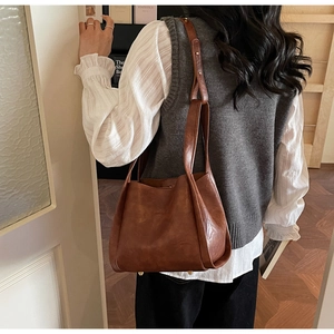 Detailed side view of brown leather bucket bag featuring gold metal protective feet