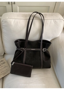Detail of a large brown suede tote bag with a matching small pouch on a cream sofa