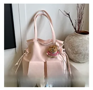 Detail of pink canvas bucket bag with drawstring pockets and a plush teddy bear charm