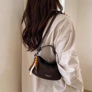Minimalist dark brown leather crossbody bag with wooden bead charms on a female model