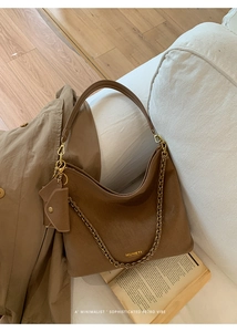 Brown faux suede tote bag with chain strap and mini pouch on a cozy white sofa