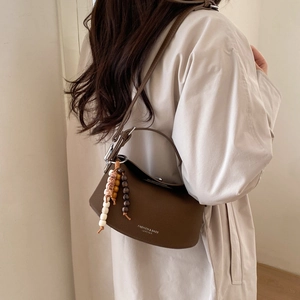 Detail of dark brown lychee leather crescent bag with adjustable strap and bead charm