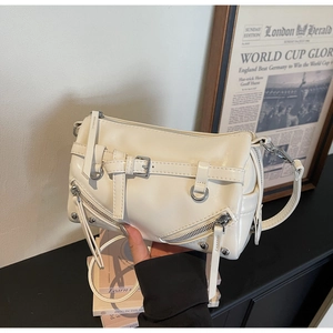 Detail shot of ivory motorcycle-style crossbody bag with silver zippers and rivets