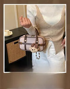 Detail of a pink pebbled leather handbag with contrast trim and cute teddy bear charm