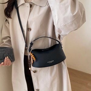 Detail of black crescent leather bag with beaded tassel worn over a beige trench coat