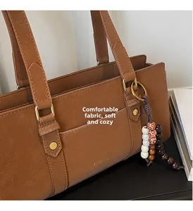 Close-up of brown textured leather bag with ethnic bead tassel and gold hardware details