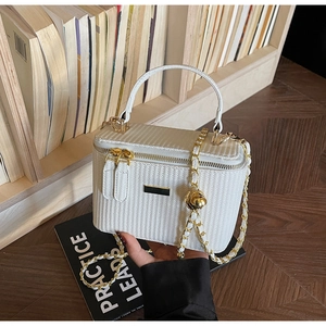 Close-up of white woven handbag with gold chain strap and metal logo on a wooden shelf