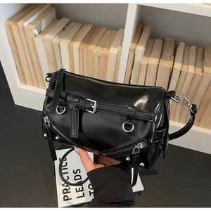 Detail of a black glossy cylinder bag with silver buckles and punk-style metal zippers