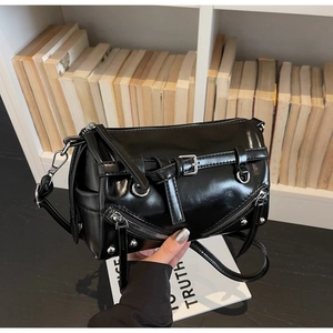 Detail view of glossy black cylinder bag featuring metallic buckles and zippers
