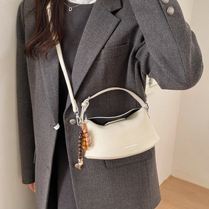 Close-up of off-white lychee grain leather bag with fashion text and bead pendant