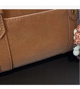 Close-up of brown textured tote bag featuring gold ZHONMA logo and wooden beaded charm