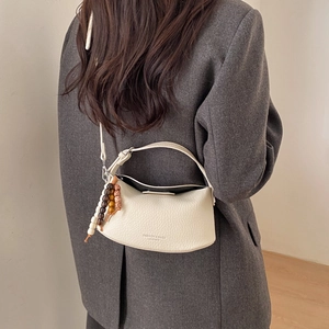 Detail of creamy white leather crescent bag with lychee texture and wooden bead charm