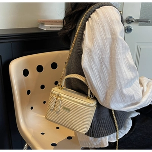 Detail of woven straw box bag with golden chain strap and top handle on a chair