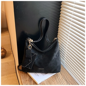 Close-up of black suede tote bag featuring contrast stitching and small pouch charm