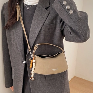 Detail of khaki leather crescent bag with wooden bead charm and printed lettering